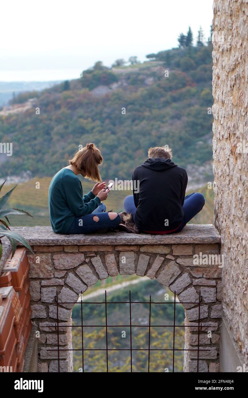 Teenager saßen auf einem Bogen. Neue Technologien und alte Architekturen. Jugendliche nutzen ihre Handys im Freien. Stockfoto