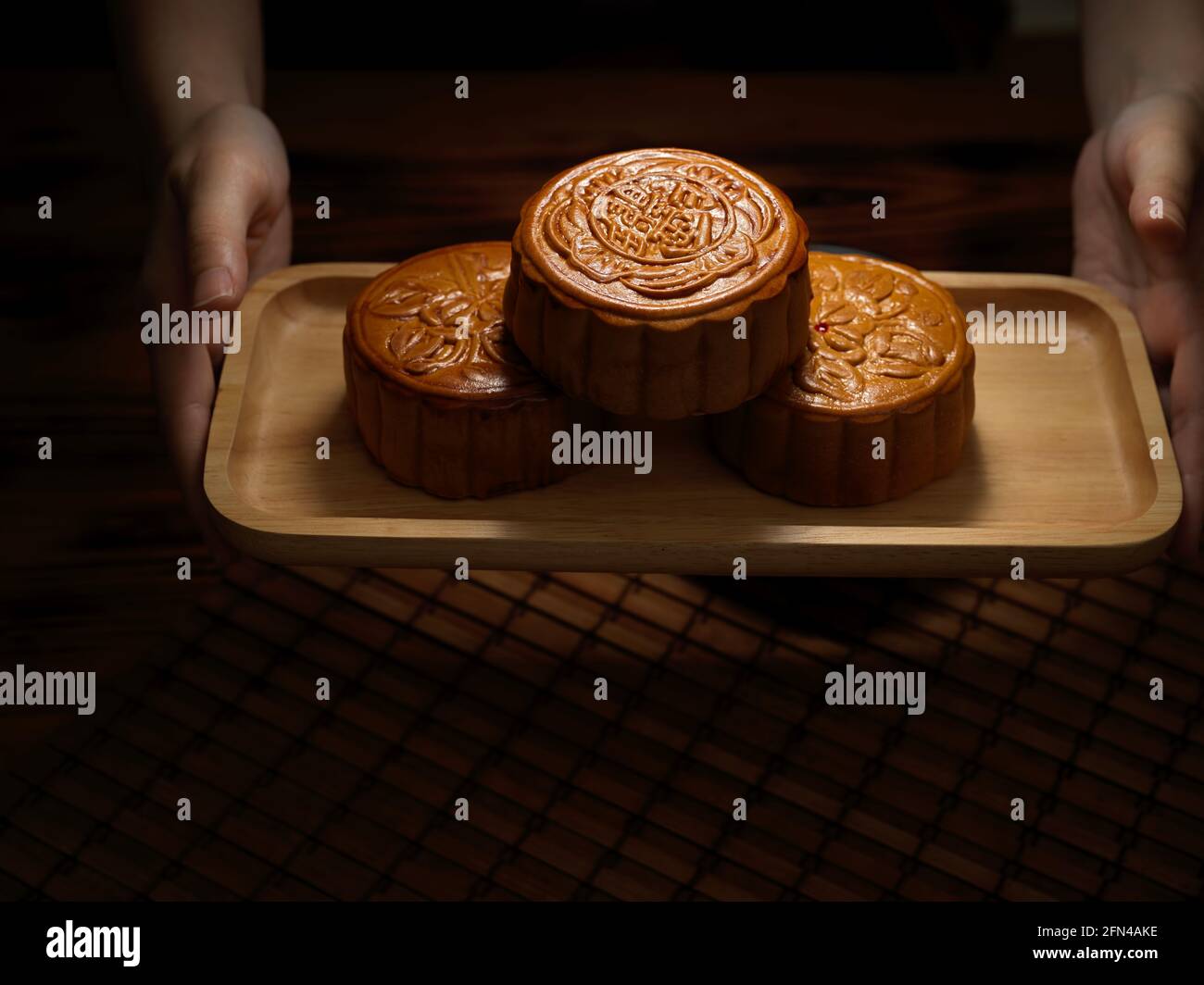 Nahaufnahme der Hände, die ein Holztablett mit traditionellen Mondkuchen halten. Chinesische Schriftzeichen auf dem Mondkuchen stehen für „fünf Kerne und Schweinebraten“ in eng Stockfoto