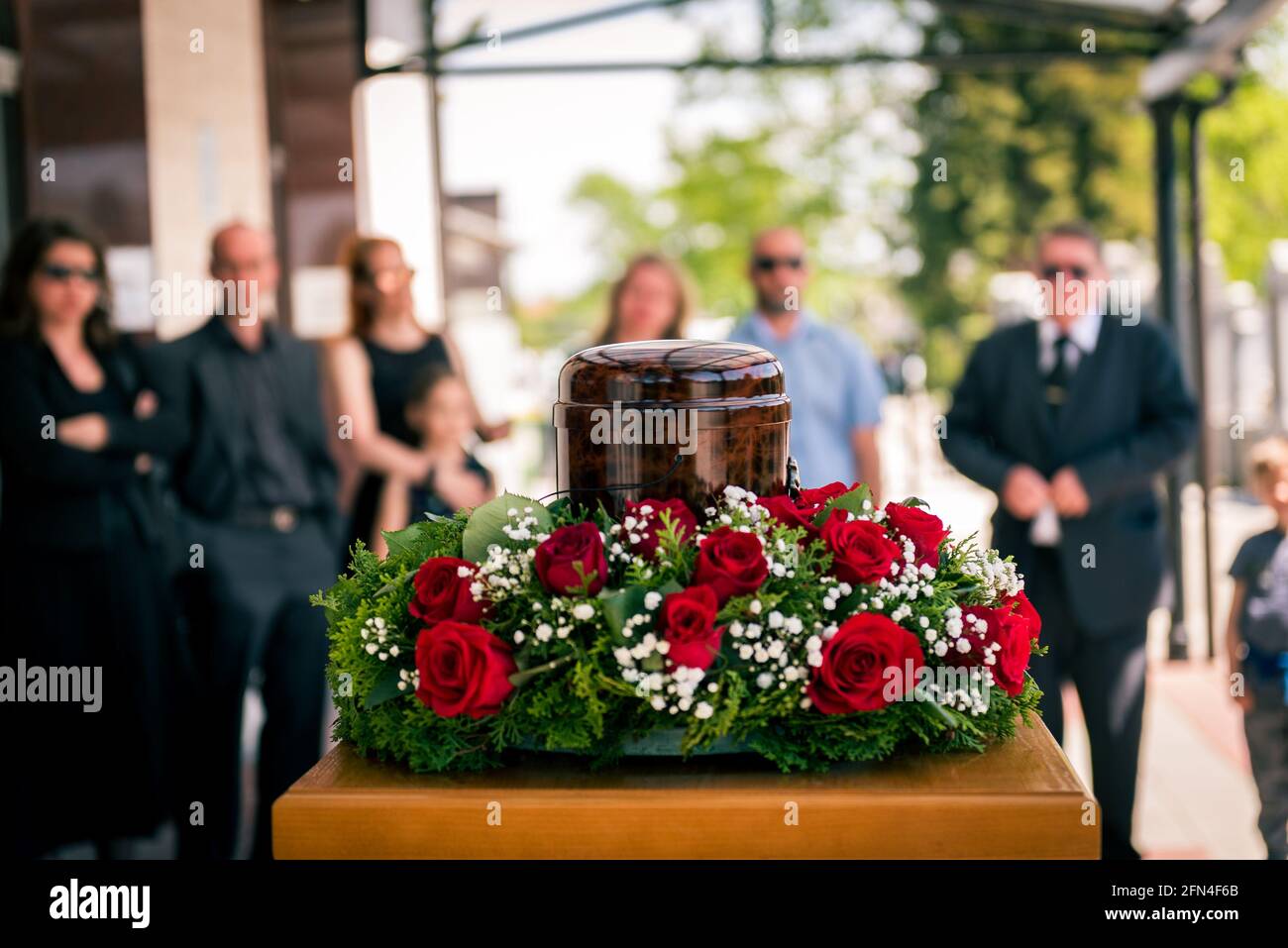 Begräbnisurne mit Asche von Toten und Blumen bei der Beerdigung. Begräbnisurne mit Blumen geschmückt und Menschen trauern im Hintergrund bei der Gedenkfeier, traurig ein Stockfoto