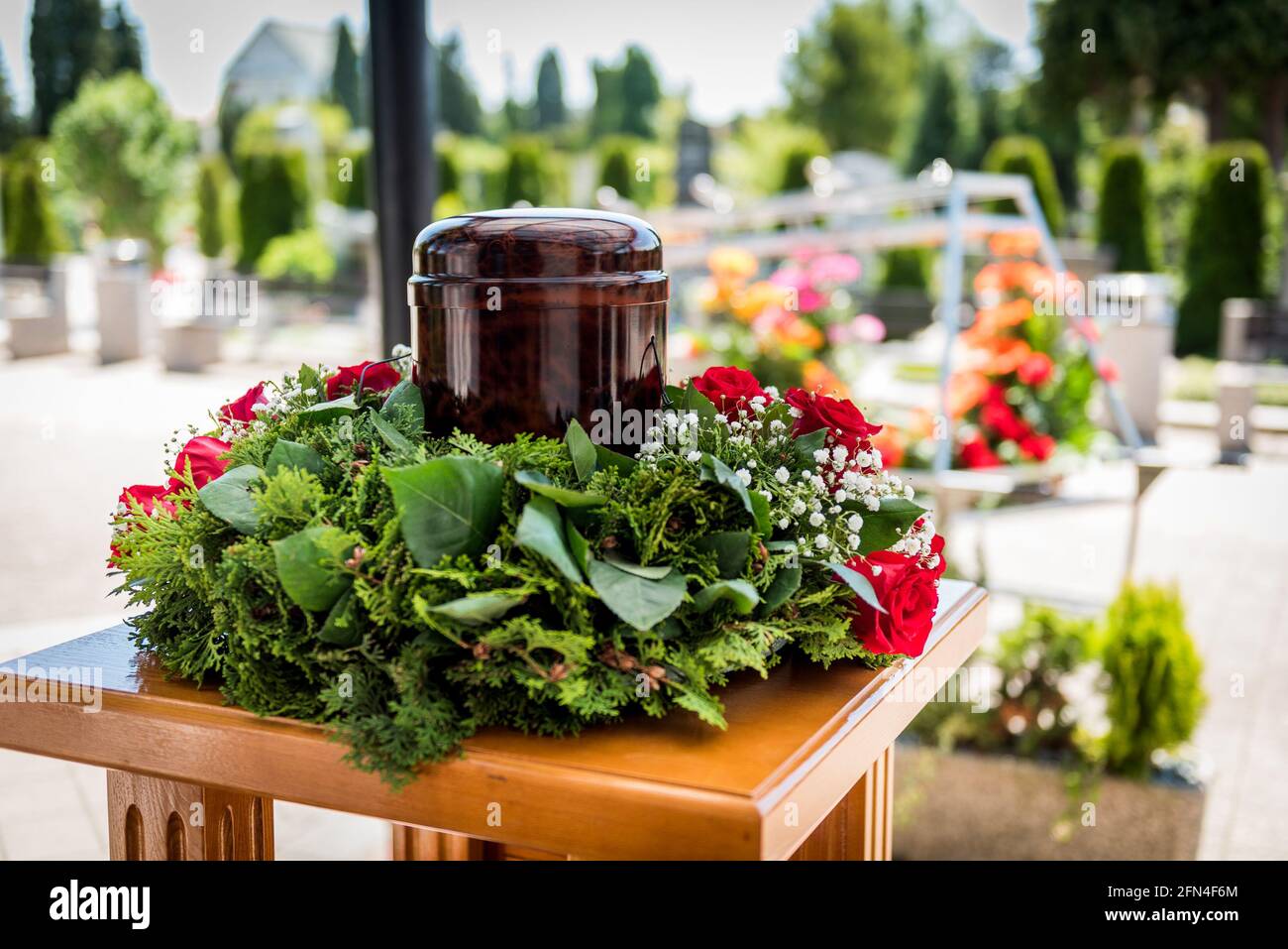 Begräbnisurne mit Asche von Toten und Blumen bei der Beerdigung. Begräbnisurne geschmückt mit Blumen und Blumenkarren im Hintergrund bei der Gedenkfeier, traurig und g Stockfoto