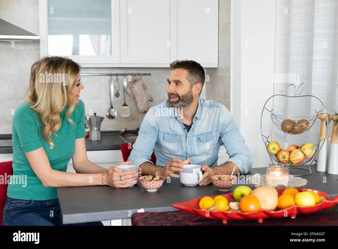 Glückliches Paar, das sich beim Frühstück unterhielt. Das Brautpaar redet beim Kaffeetrinken am Küchentisch. Lächeln, Lifestyle und Happy Morning. Stockfoto