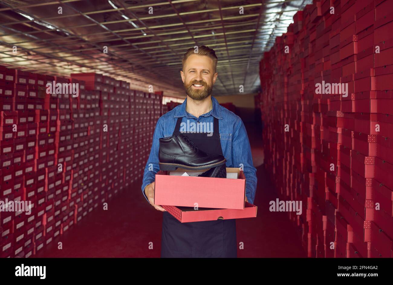 Glücklicher Schuhfabrikbesitzer oder Lagerverwalter, der einen Karton hält Mit schwarzen Lederstiefeln Stockfoto