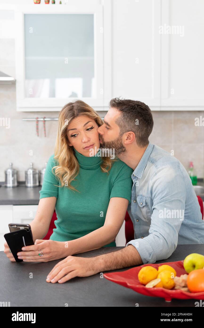 Die blonde Frau macht ein Selfie, während sie von ihrem Freund geküsst wird. Mädchen mit grünem Hemd fotografiert sich für soziale Medien. Glückliches Paar. Stockfoto