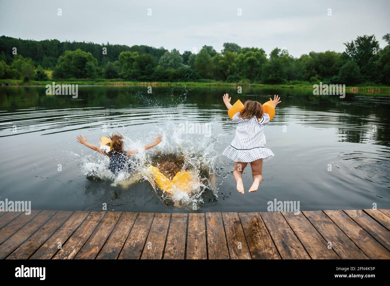 Kleine Mädchen, die Spaß auf einem See springen in die Wasser von der Holzterrasse, die im Sommer Party-Kleider trägt Feiertage Stockfoto