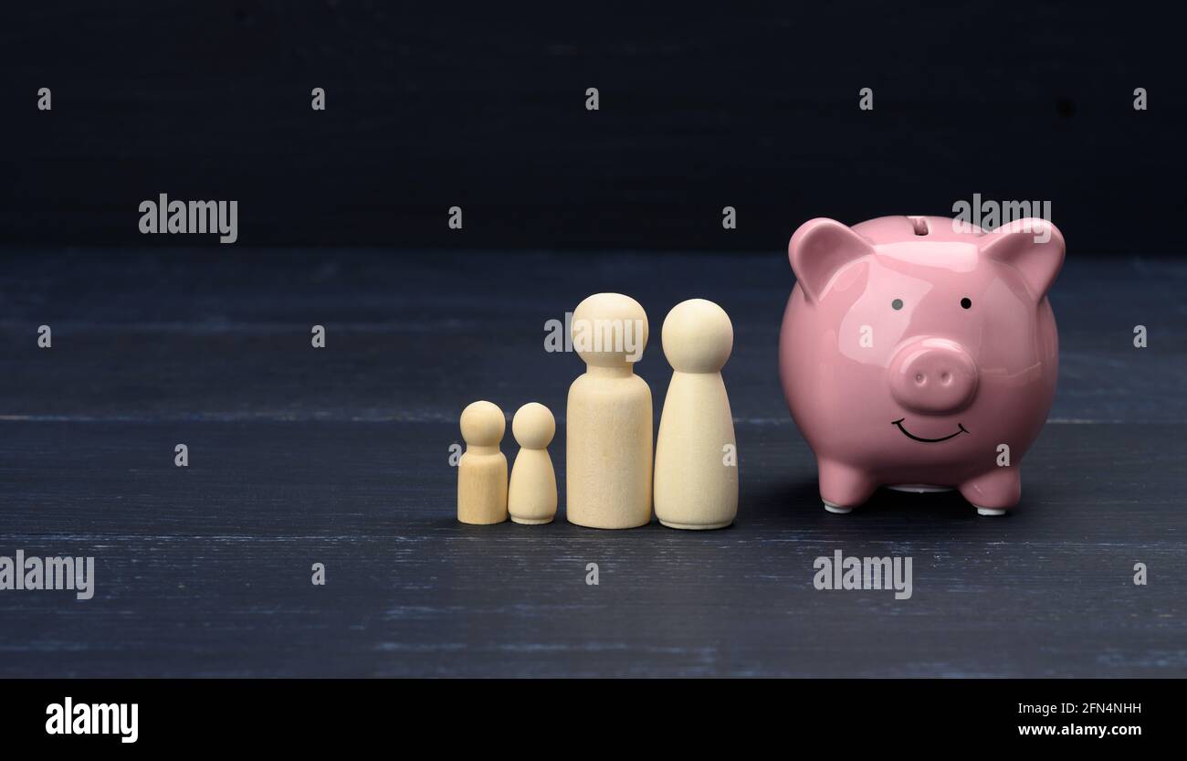 Hölzerne Familienfiguren und rosa Keramik Sparschwein, Sparkonzept, Budgetkontrolle. Langfristige Planung der Verteilung der Mittel für große Käuferzahlen Stockfoto