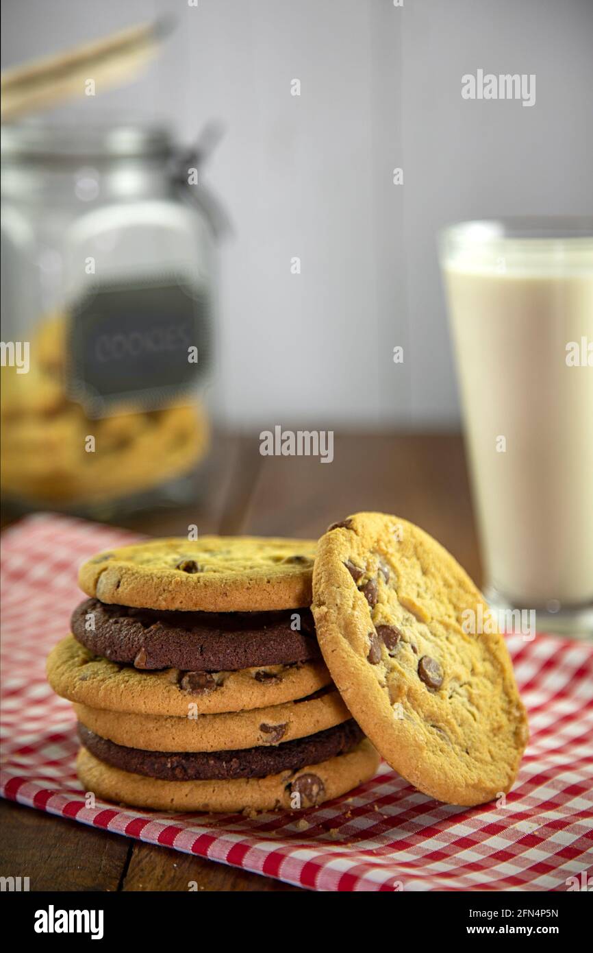 Stapel Schokoladenkekse auf rotem Gingham-Tuch mit Glas Von Milch und Keksdose Stockfoto