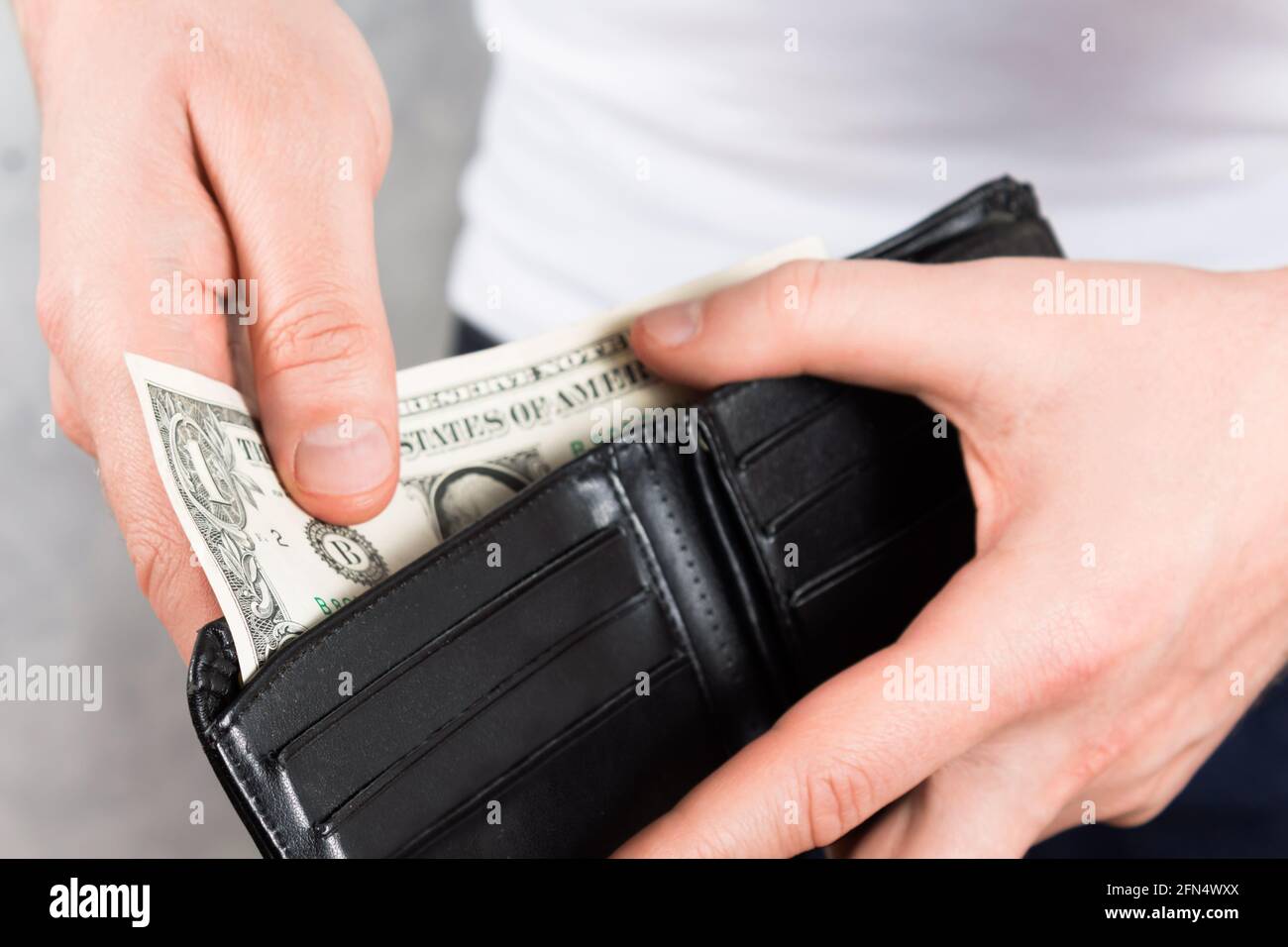 Nicht erkennbarer junger Mann, der eine schwarze Lederbörse mit zwei Dollar in den Händen hält. Nahaufnahme des Fotos. Konzept der Finanzkrise. Stockfoto