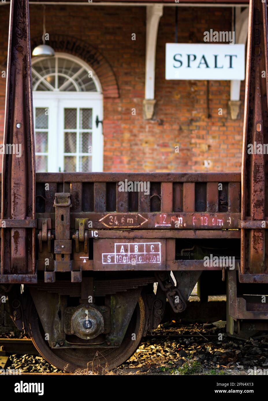SPALT IN BAYERN, DEUTSCHLAND - 07. Mai 2021: Im Vordergrund ein alter rostiger Güterwagen mit weißer Schrift. Im Hintergrund ein stillgeruhrter Bahnhof i Stockfoto