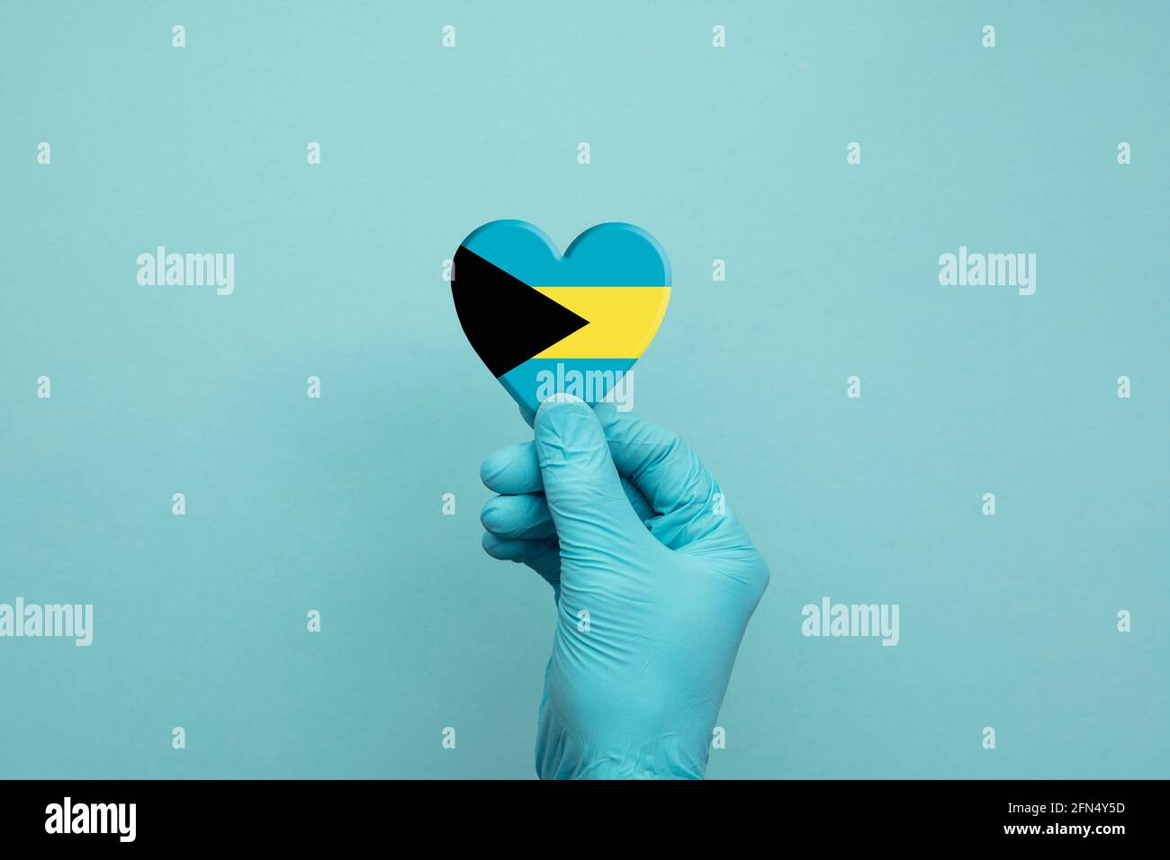 Hände mit schützenden chirurgischen Handschuhen, die das Herz der Bahamas-Flagge halten Stockfoto