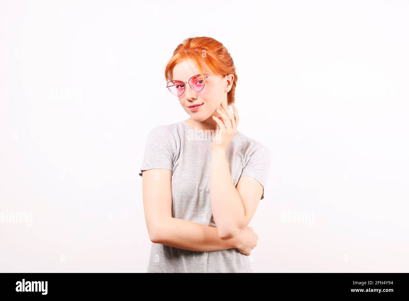 Attraktive junge Frau mit langen roten Haaren, trägt eine rosa Katzenaugen-Sonnenbrille, zeigt flirtatious Körpersprache, berührt das Gesicht. Schönes Rothaarweibchen Stockfoto