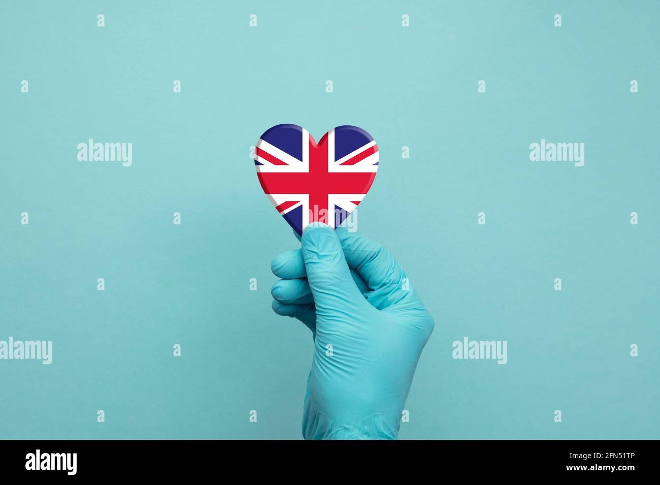 Hände mit schützenden chirurgischen Handschuhen, die das Herz der britischen Flagge halten Stockfoto