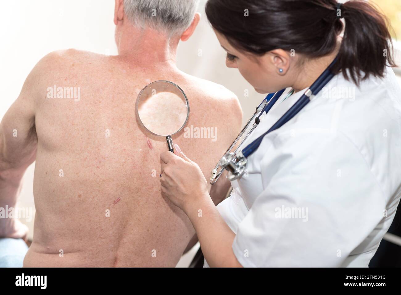 Junge Ärztin, die die Haut eines älteren Patienten untersucht Stockfoto
