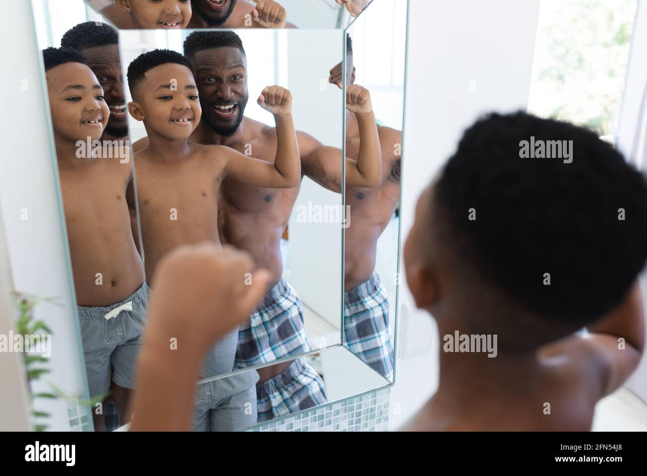 afroamerikanischer Vater und Sohn im Badezimmer, im Spiegel schauend, Muskeln zeigend Stockfoto