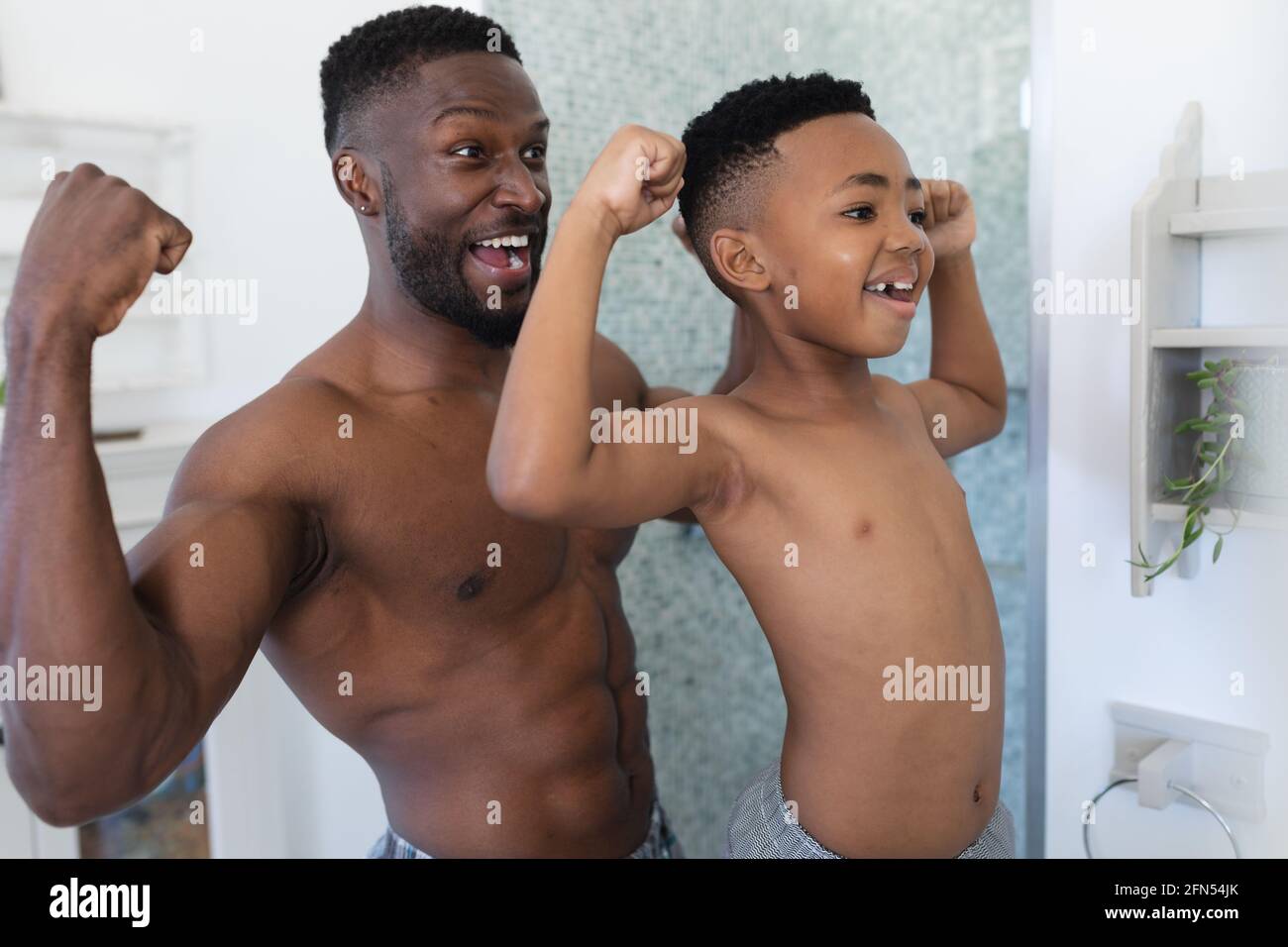 afroamerikanischer Vater und Sohn im Badezimmer, im Spiegel schauend, Muskeln zeigend Stockfoto