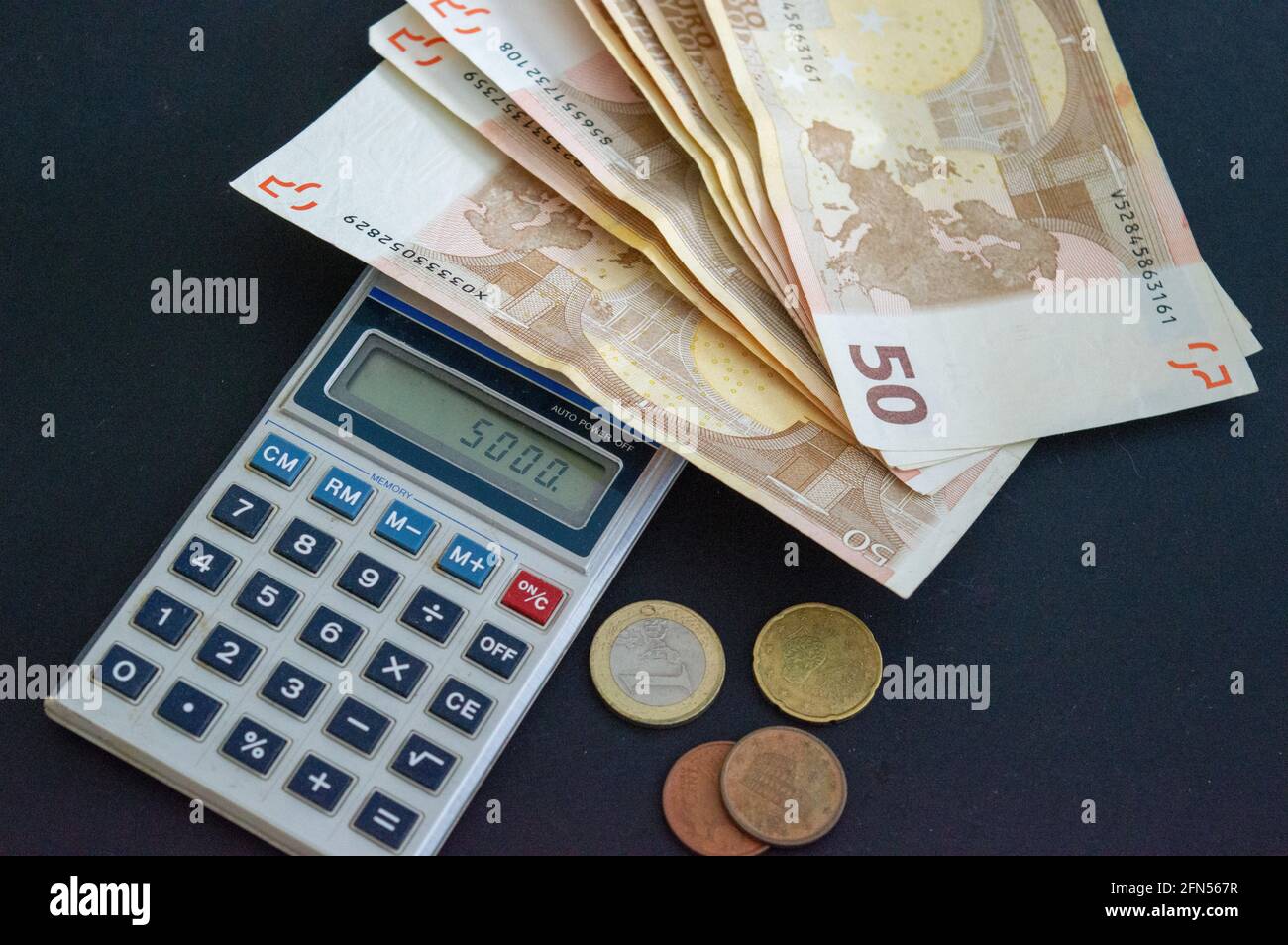 Taschenrechner mit 50-Euro-Banknoten und -Münzen auf grau-schwarzem Hintergrund. Stockfoto