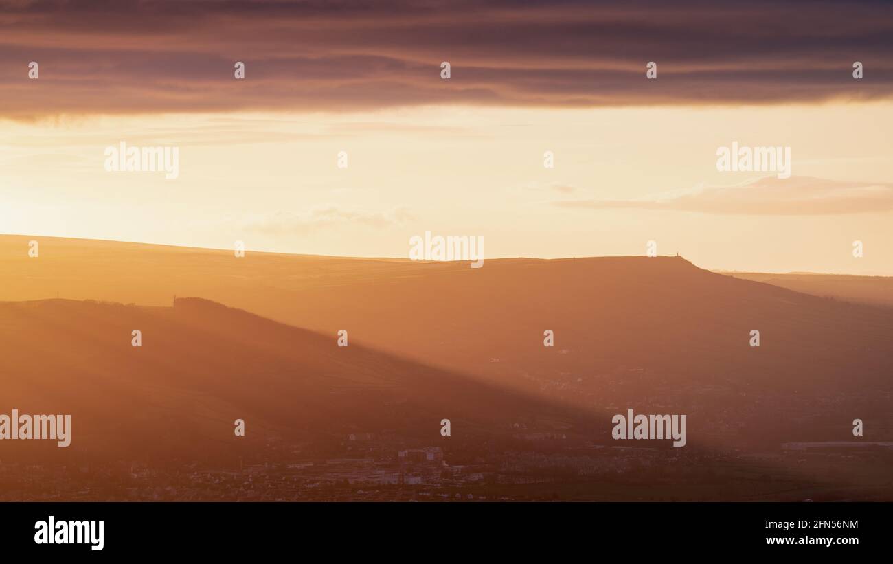 Dramatische Lichtstrahlen beleuchten das Aire Valley, wenn die untergehende Sonne unter eine brütende Wolkenbank fällt. Wainmans Spitze ist am Horizont sichtbar. Stockfoto