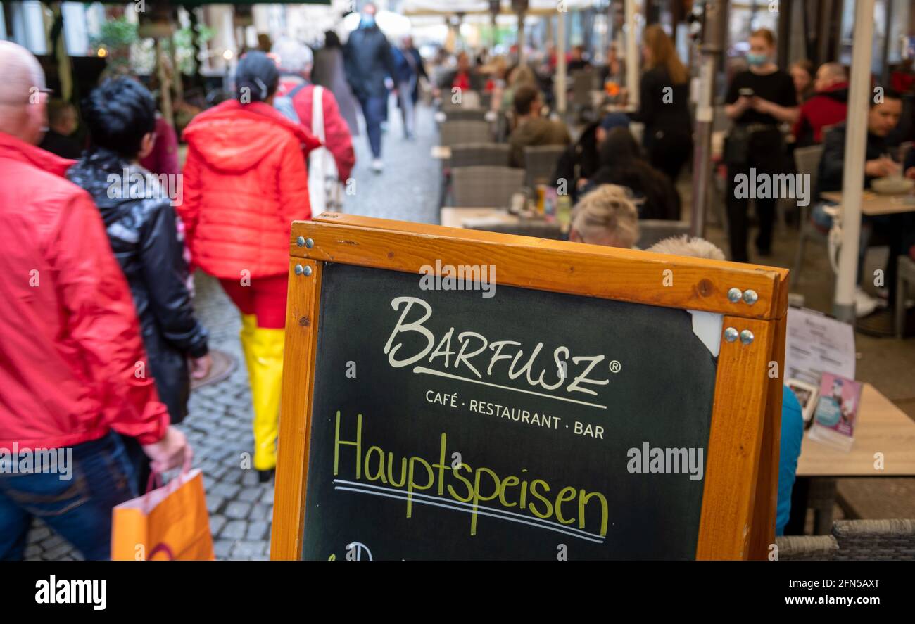 Leipzig, Deutschland. Mai 2021. Passanten gehen durch die Barfußgasse an den gut besuchten Sitzgelegenheiten im Freien der Bars und Restaurants vorbei. Die Rückkehr der Outdoor-Gastronomie hat begonnen. Ab heute dürfen Gastronomen in der Messestadt wieder Speisen und Getränke im Freien servieren. Leipzig liegt derzeit deutlich unter der kritischen Inzidenzmarke von 100. Quelle: Hendrik Schmidt/dpa-Zentralbild/dpa/Alamy Live News Stockfoto