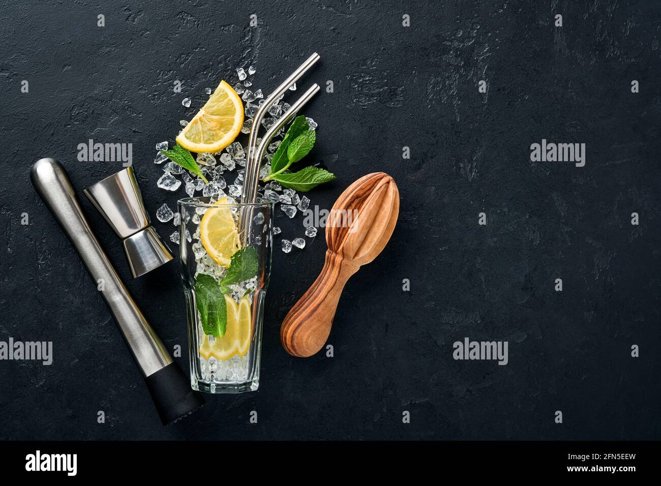 Mojito oder Lemonade Cocktail im Longdrinkglas mit Eiswürfeln, Minze und Limette auf schwarzem Steingrund mit Shaker und Becher. Menüleiste. Platz für Text Stockfoto
