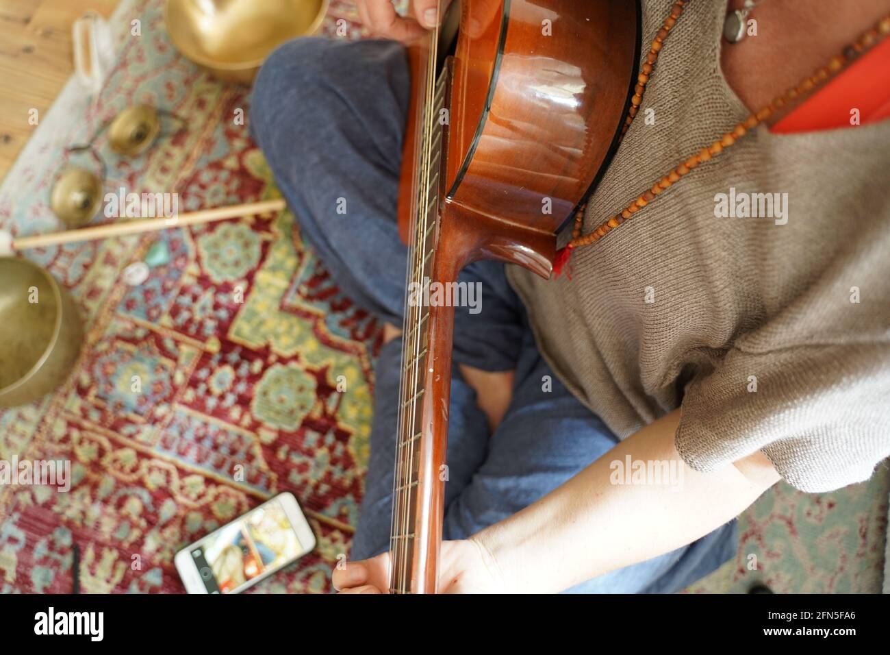 Mädchen mit Gitarre sitzt auf dem Boden in Yogi-Pose. Stockfoto