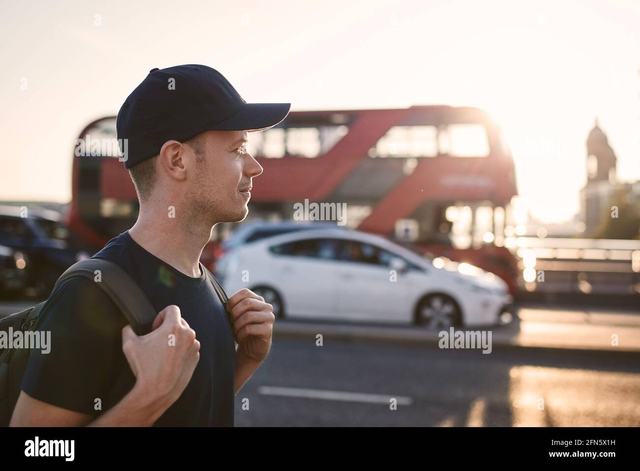 Porträt eines fröhlichen Mannes auf der Straße der Stadt. Tourist gegen Bus der öffentlichen Verkehrsmittel bei schönem Sonnenuntergang. London, Großbritannien Stockfoto