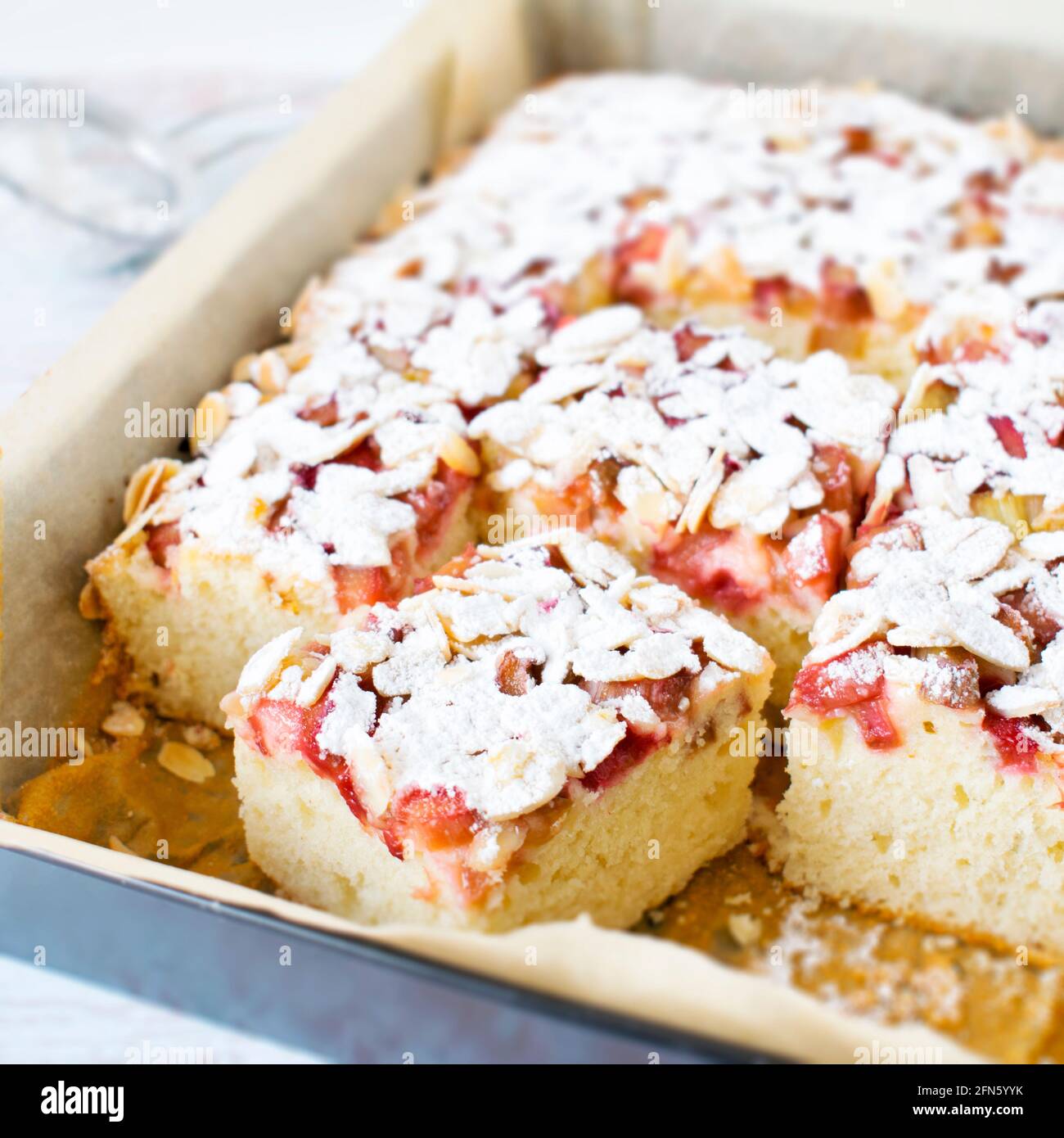 Hausgemachter Kuchen - Joghurtkuchen mit Rhabarber, bestreut mit Mandelflocken und Puderzucker. Stockfoto