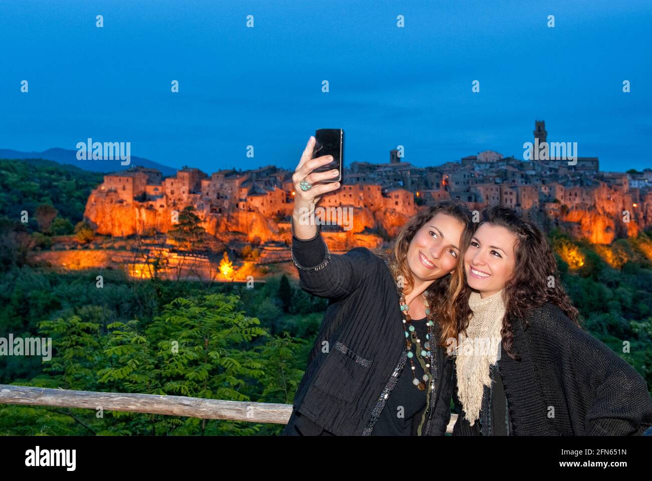 Frauen, die bei Sonnenuntergang ein Selfie mit der mittelalterlichen Stadt Pitigliano machen. Stockfoto