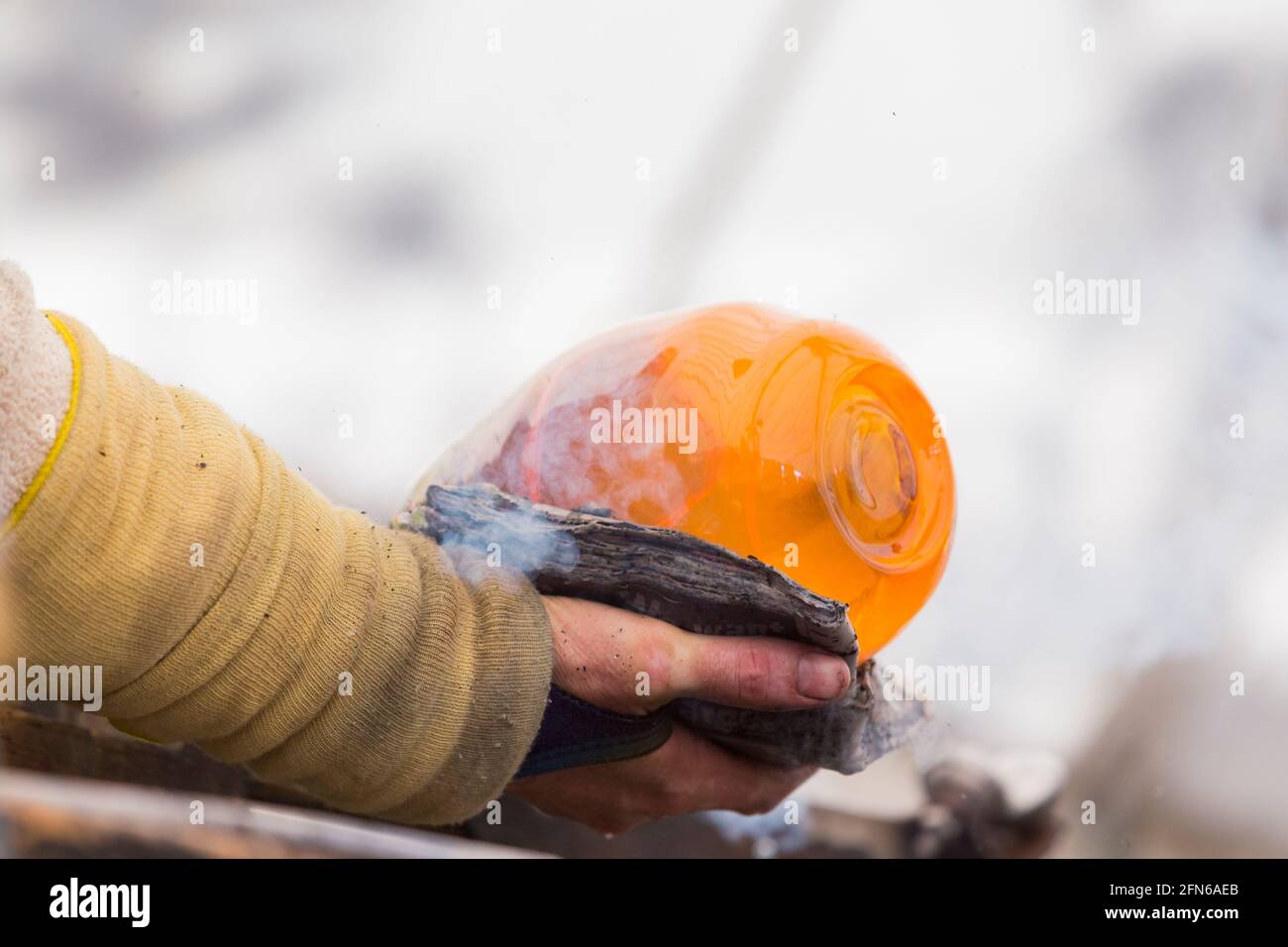 Ein Glasbläser verwendet nass gefaltete Zeitungen als Wärmeschutzisolierung, während er mit der Hand geschmolzenes Glas auf seinem Blasrohr dreht und formt. VEREINIGTES KÖNIGREICH (123) Stockfoto