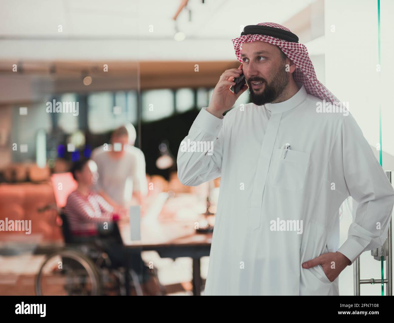Nahöstlicher arabischer Geschäftsmann im Büro, der auf dem Smartphone spricht Vor seinem Team Stockfoto