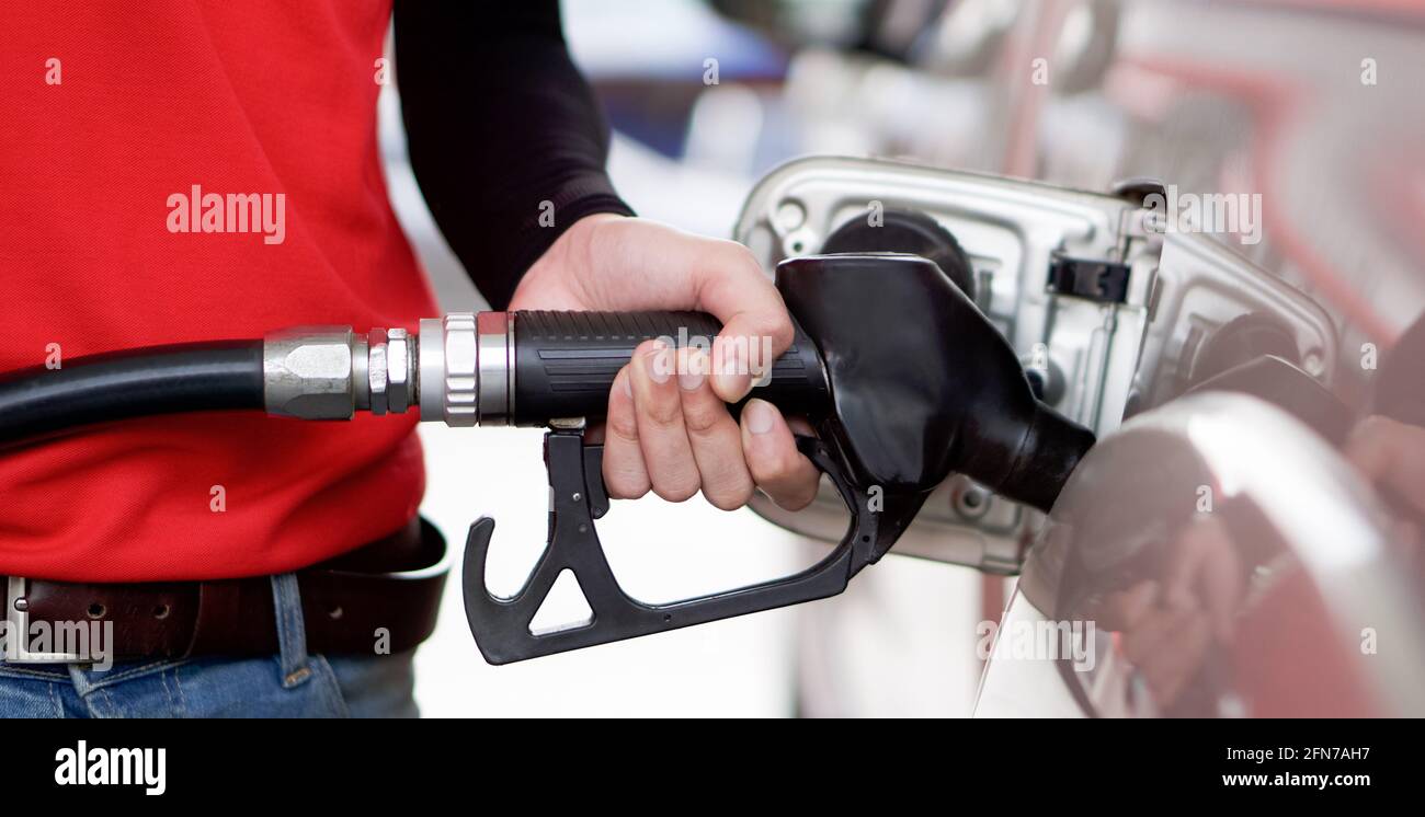 Tankstellenmitarbeiter in roter Uniform füllen Bronze Pickup LKW-Tank. Nahaufnahme Hand mit schwarzer Gaspumpendüse. Stockfoto