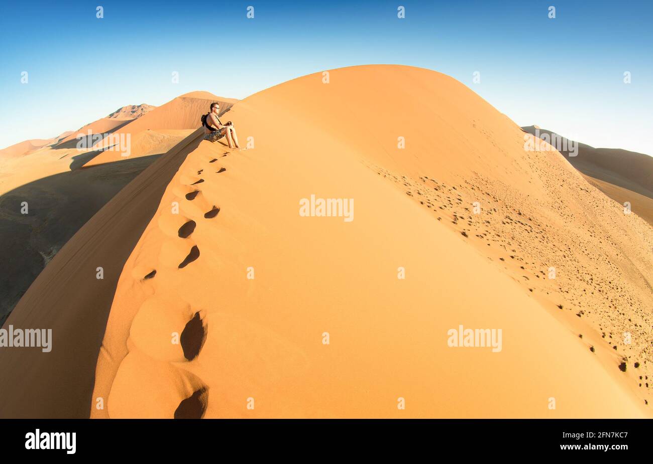 Einsamer Mann, der auf Sand in der Dune 45 in Sossusvlei sitzt - Konzept der Fernweh in namibischer berühmter Wüste - Abenteuer Reise nach african Wonders Stockfoto