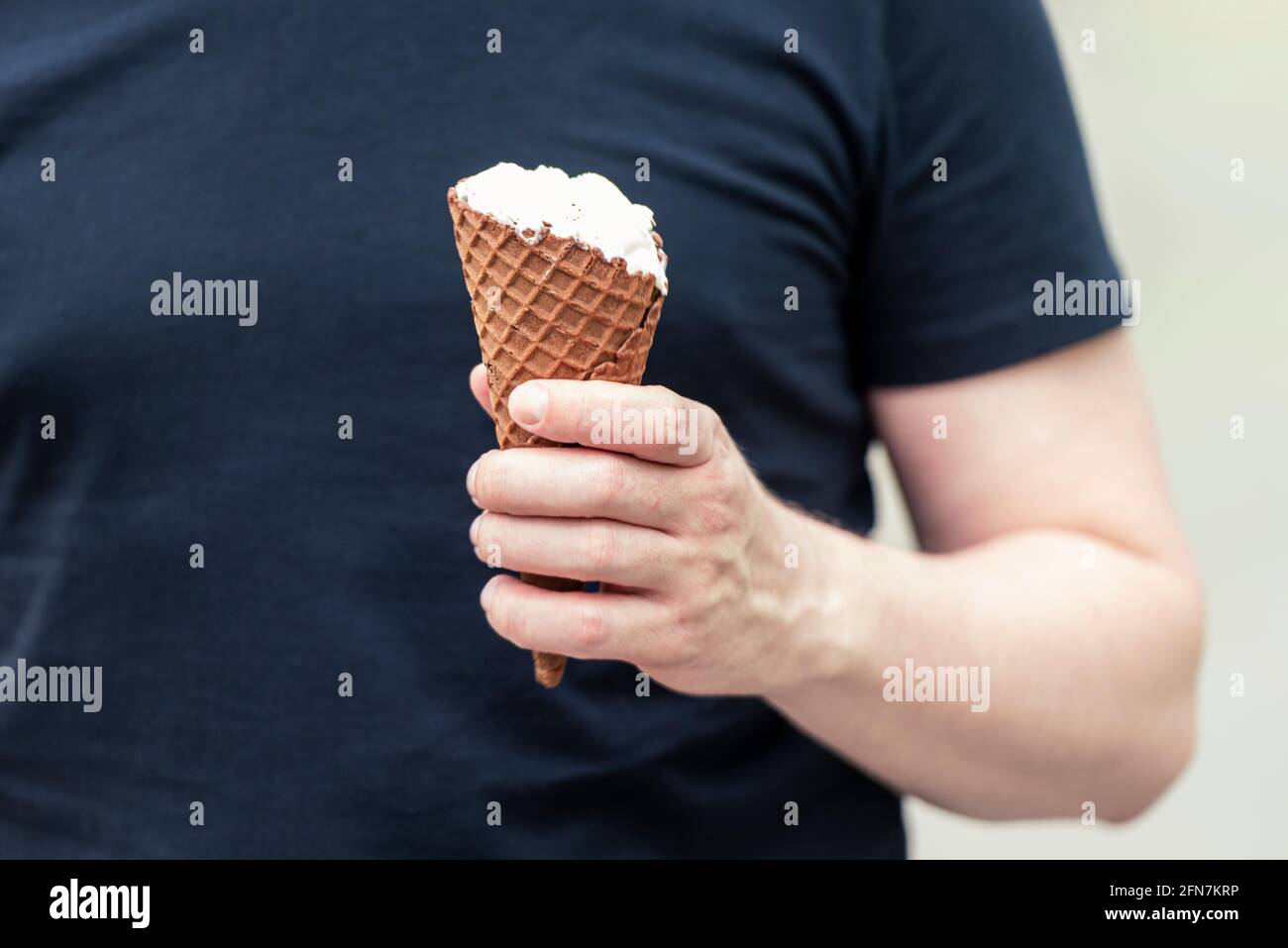 Ein brutaler Mann in schwarzem T-Shirt mit einem Eis Creme in der Hand in einem Stadtpark Stockfoto