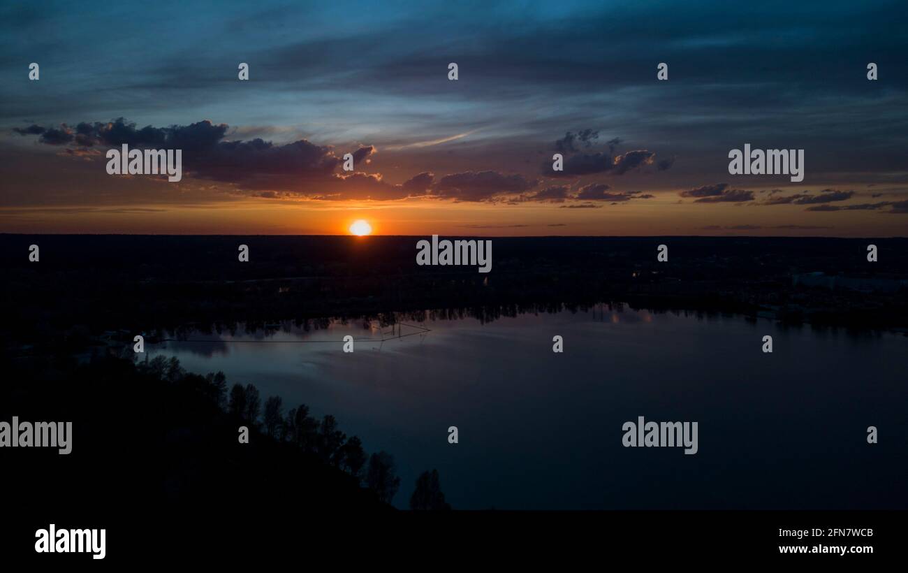 Schöner Sonnenuntergang mit Wolken über dem Fluss unter Bau Häuser in der Dunkelheit, Ukraine, Kiew am 6. Mai. Stockfoto