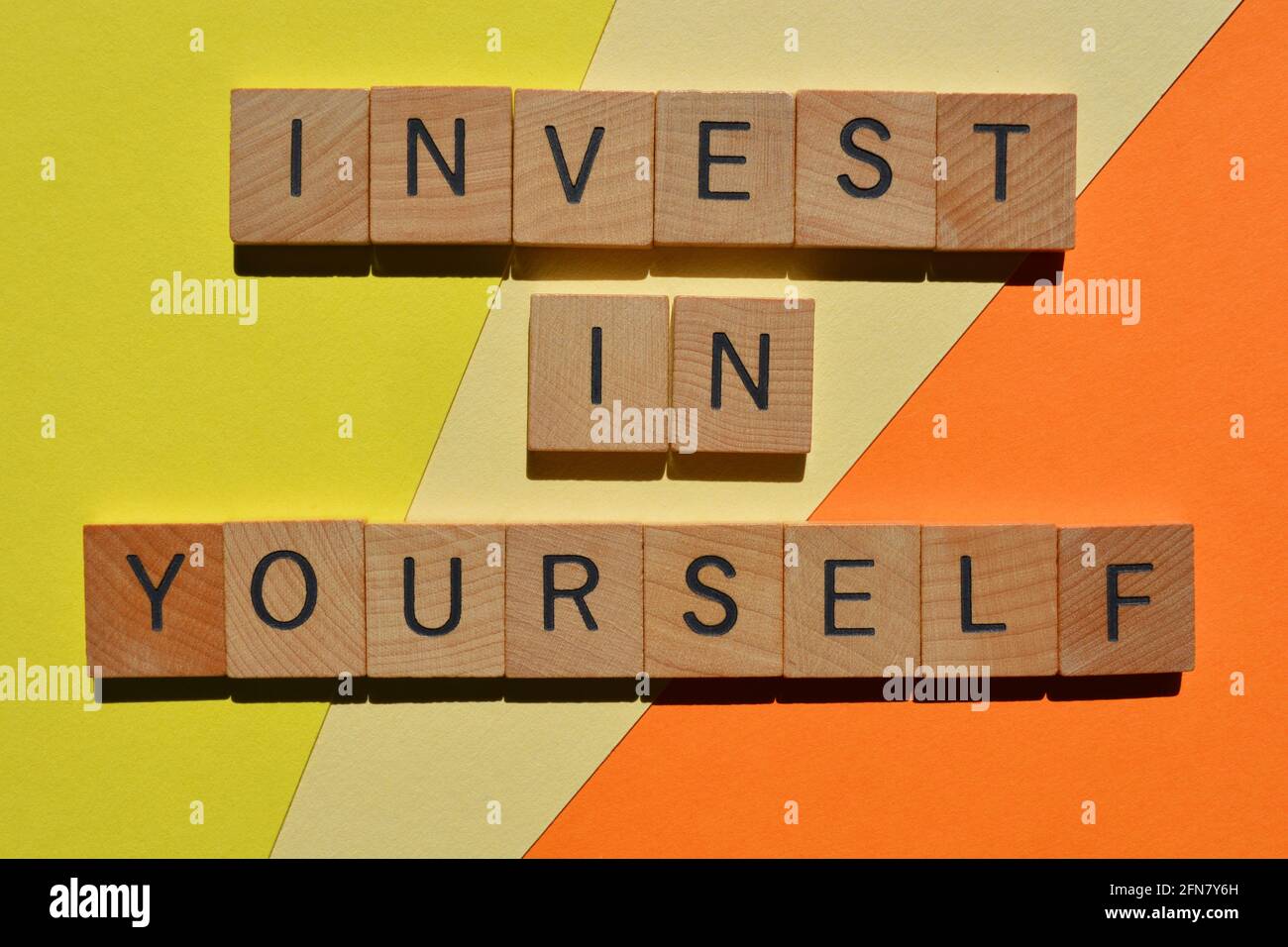 Investieren Sie in sich selbst, Ausdruck in hölzernen Buchstaben auf buntem Hintergrund isoliert Stockfoto