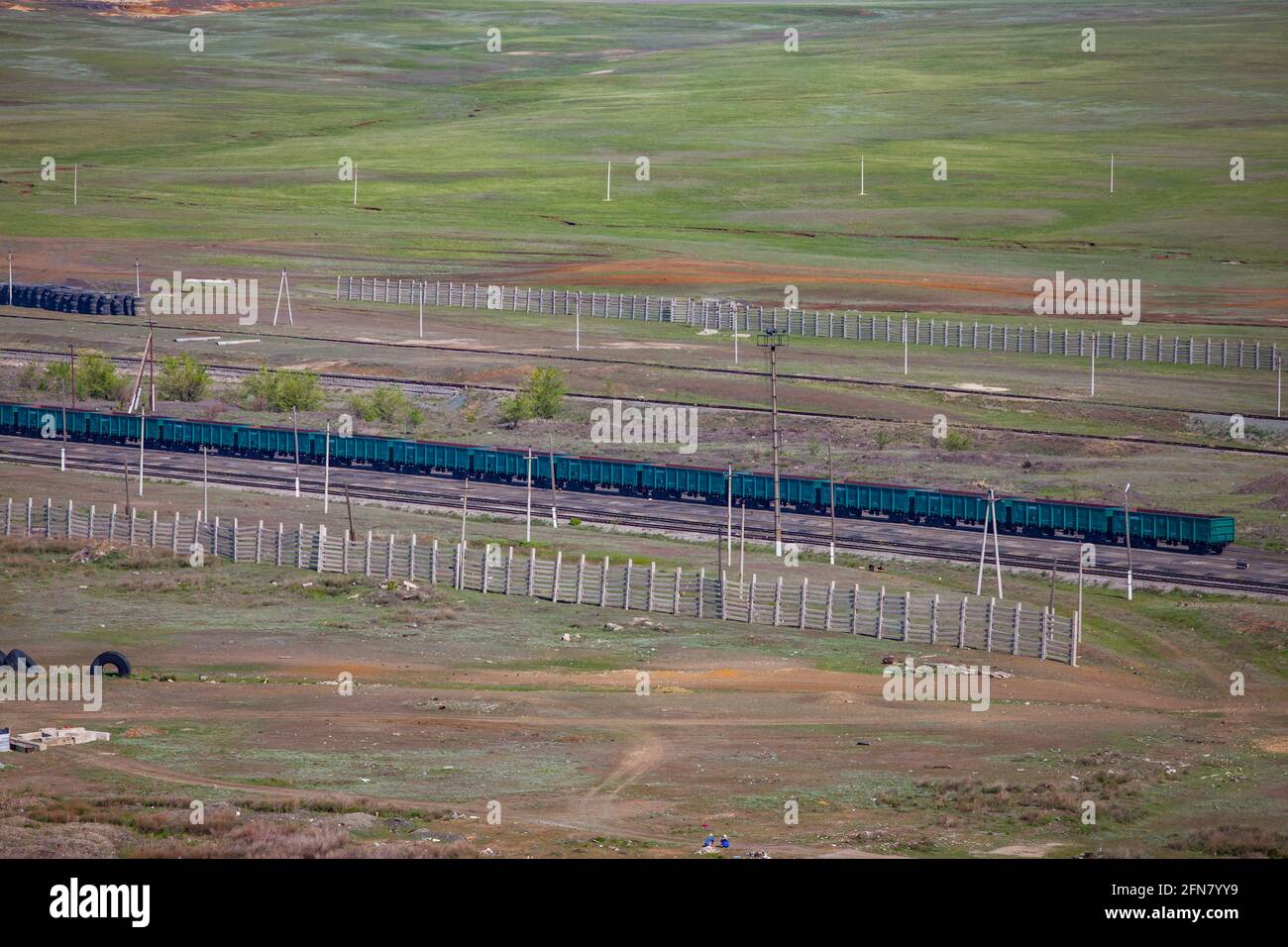 Luftaufnahme auf Geen Zug offenen Waggons in grüner Steppe. Graue Schneezäune. Graue Betonmasten. Stockfoto