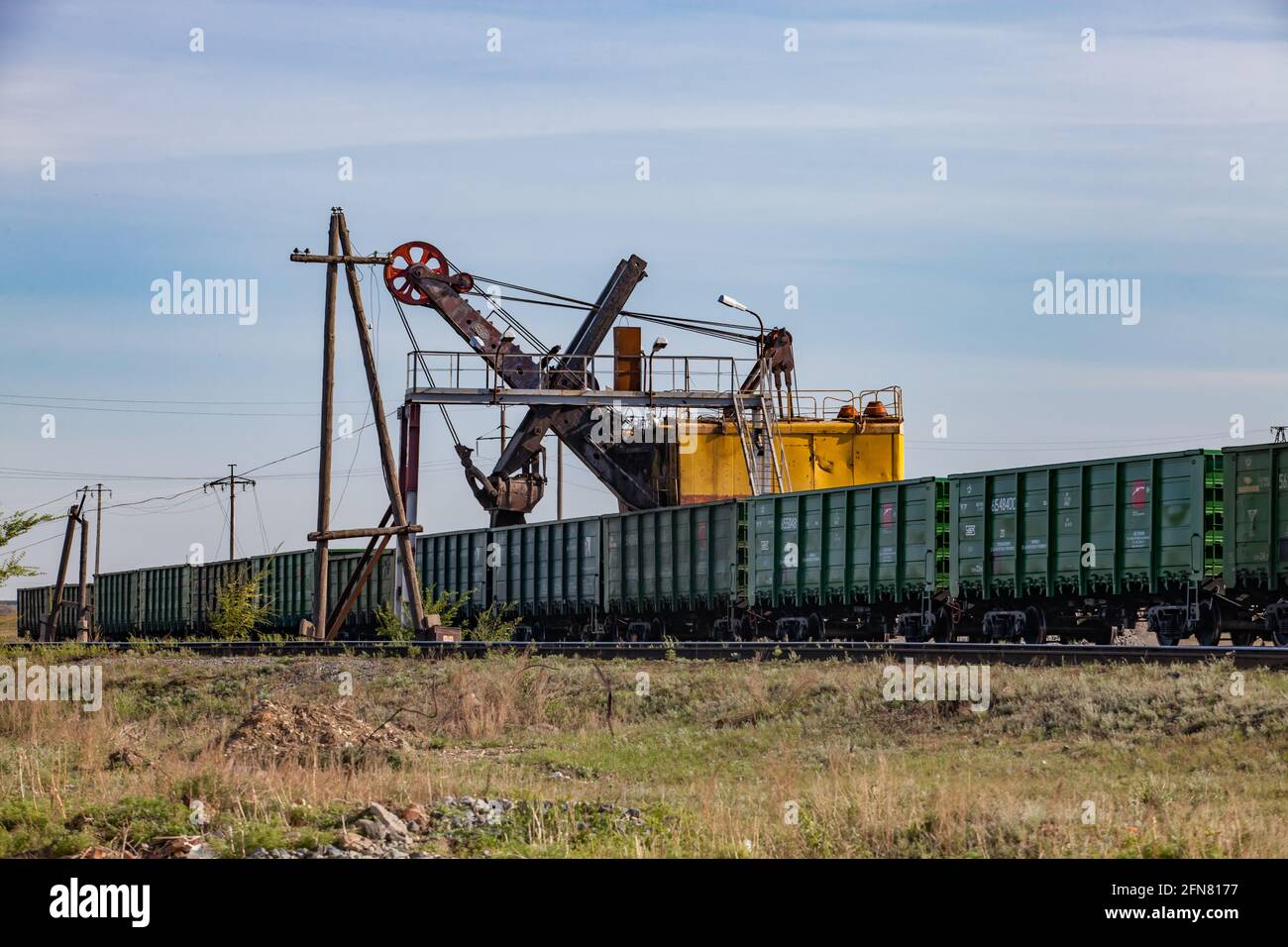 Khromtau, Kasachstan. Erzladestation. Bagger belädt offene Wagen. Brücke und Holz elektrische Stange. Wüstensand und Gras. Stockfoto