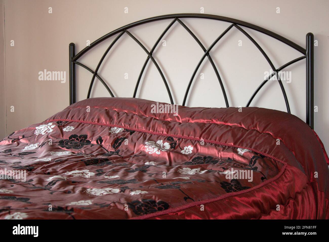 Doppelbett mit Kopfteil aus schwarzem Metall und schwarz-rot Seidige Bettdecke Stockfoto