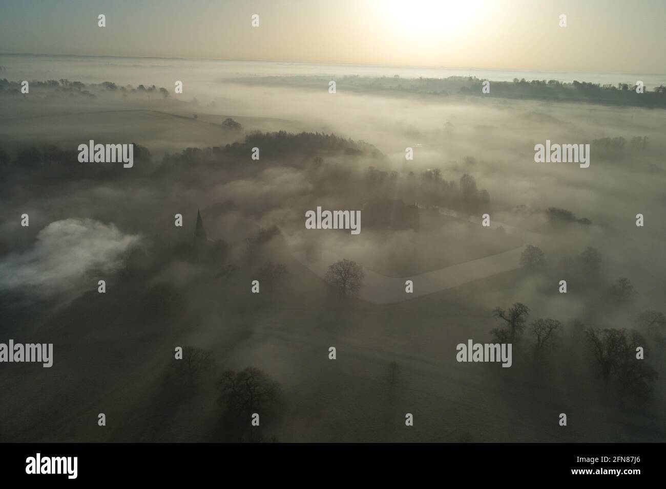 Dramatische atmosphärische Drohnenaufnahme von Broughton Castle and Estate bei Sonnenaufgang bedeckt mit Lichtung, die aus Nebel und Nebel auftaucht Stockfoto