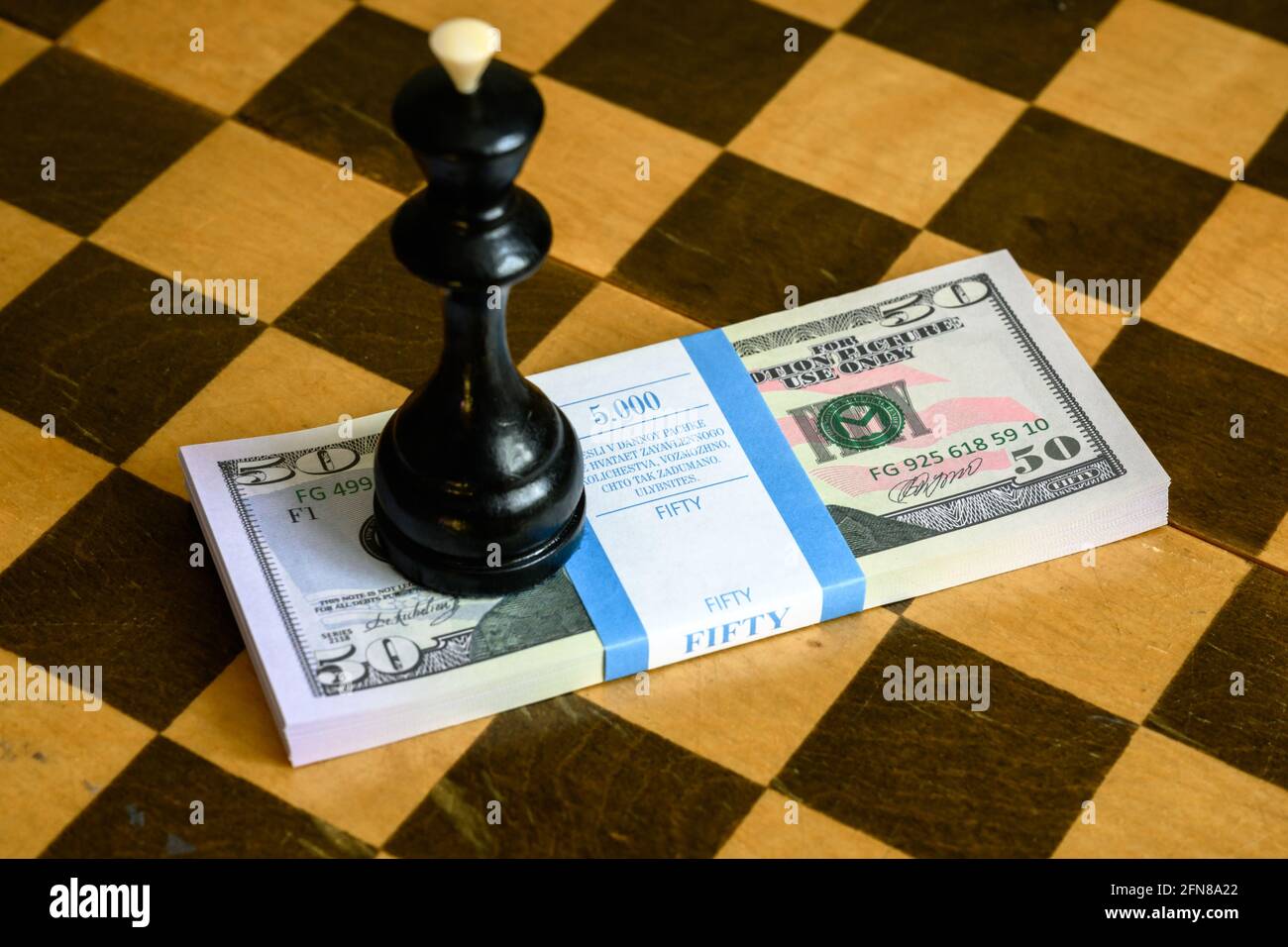 Schachkönig und Dollarscheine stapeln sich auf Schachbrett, US-Papierwährung und Spiel. Konzept von Geldstrategie, unlauterem Wettbewerb, Wetten, Sportwetten, Gamb Stockfoto