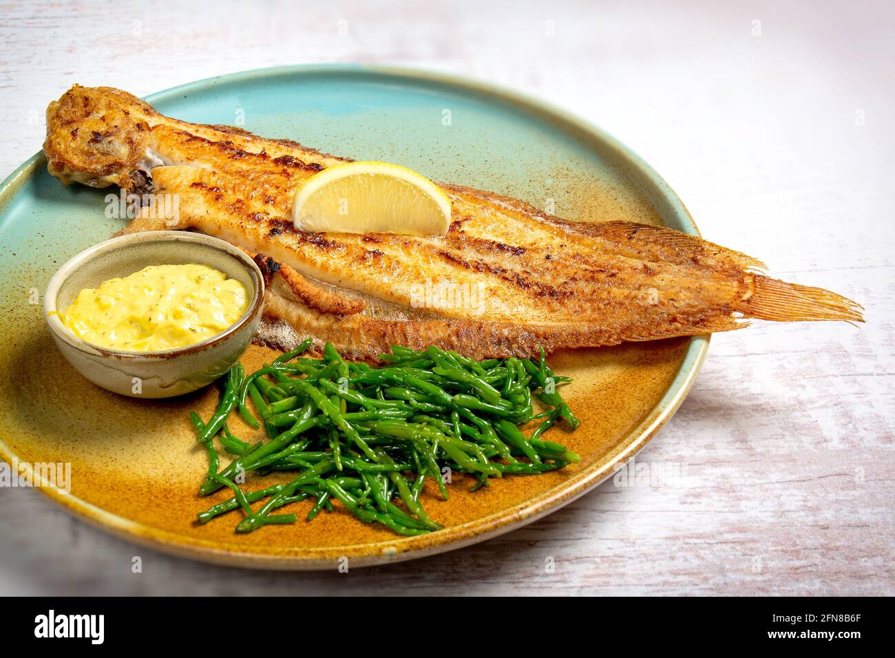 Gebackene ganze Flunder Fisch serviert auf einem bunten Teller mit Zitrone, Samphire und Buttersauce Stockfoto