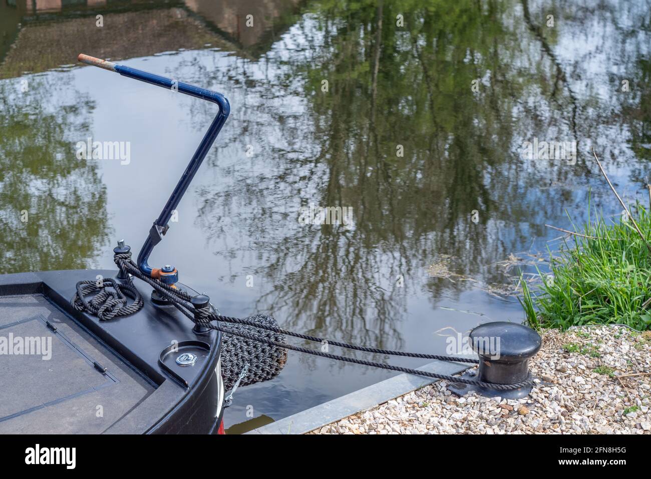 Stern eines verankerten Kanalbootes mit gewebtem Seilstoßfänger und blauer Metallstange. Stockfoto