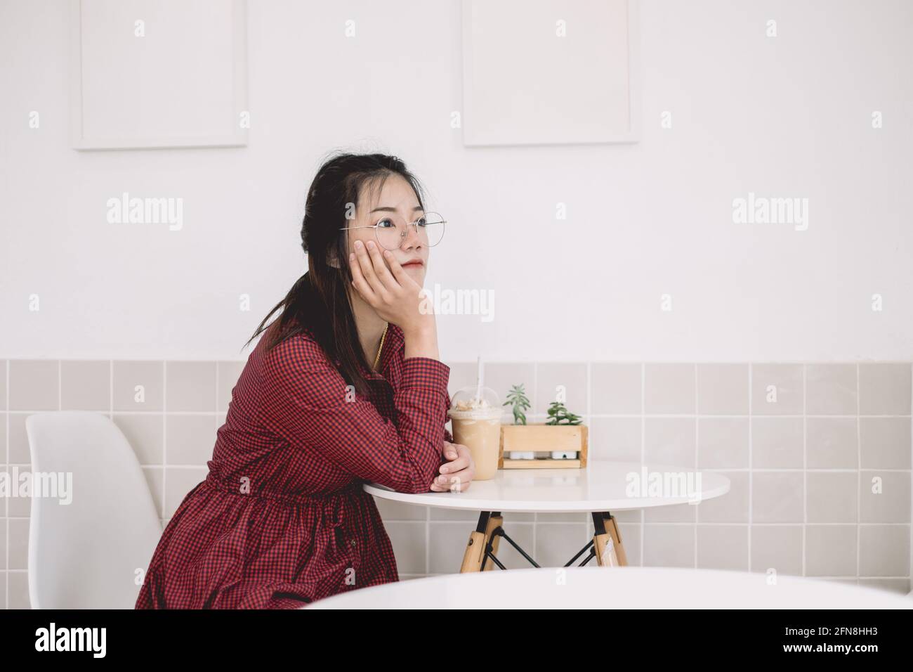 Asiatische Mädchen teen sitzen denkenden Tag Traum langweilig und nachdenklich Blick weg in weißen Café allein. Stockfoto