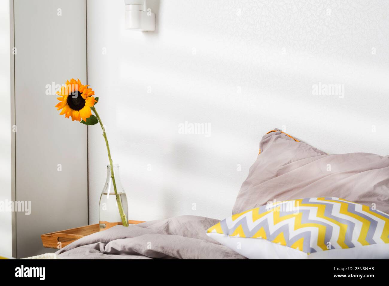 Einzelne schöne gelbe Sonnenblume in Vase in der Nähe des Bettes im Schlafzimmer Stockfoto