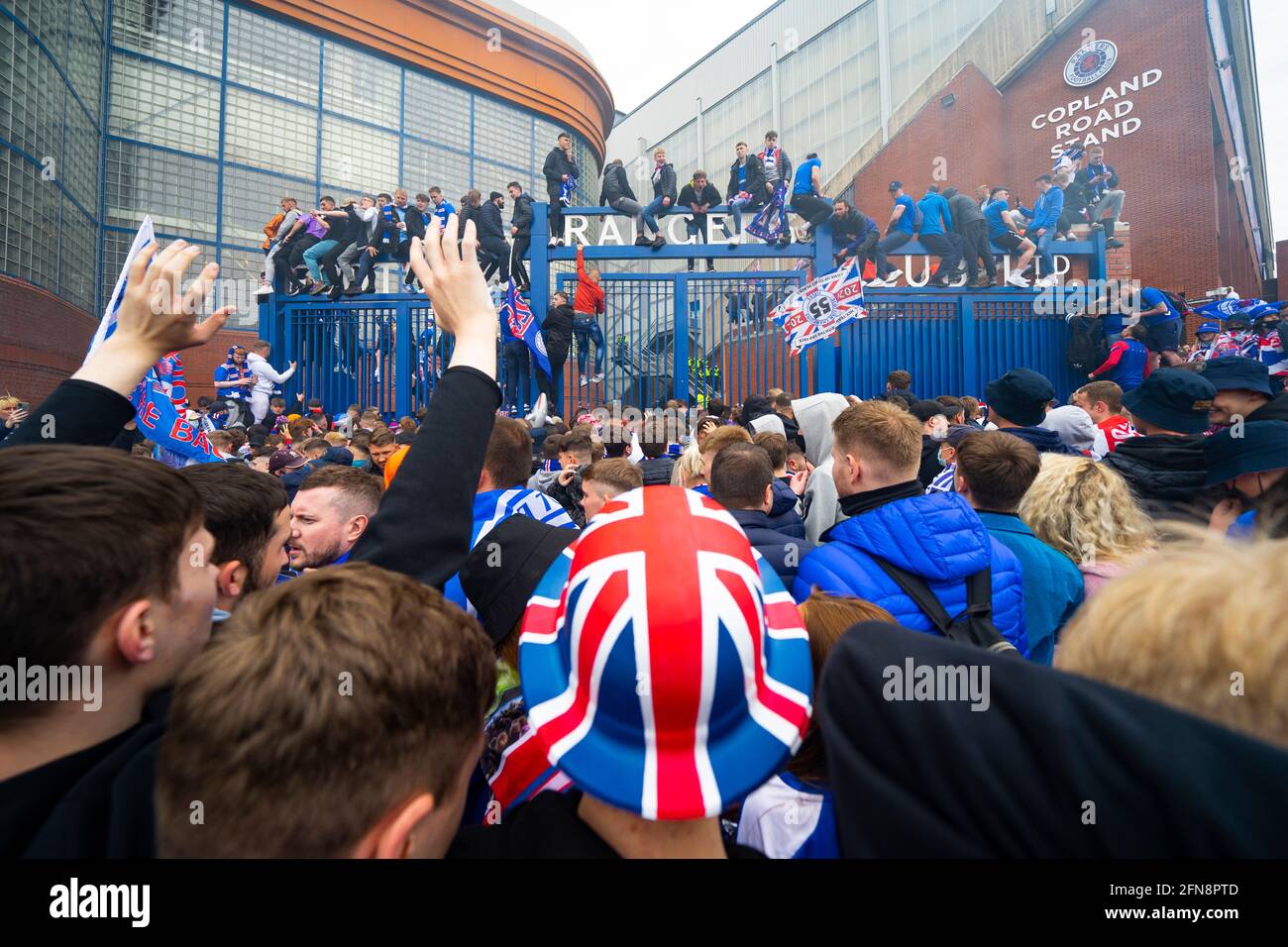 Glasgow, Schottland, Großbritannien. 15 Mai 2021. Tausende von Fans und Fans des Rangers-Fußballvereins kommen im Ibrox Park in Glasgow zusammen, um den Sieg der schottischen Premiership-Meisterschaft zum 55. Mal und zum ersten Mal seit 10 Jahren zu feiern. Rauchbomben und Feuerwerk werden von Fans, die von der Polizei streng kontrolliert werden, weg von den Eingängen des Stadions losgelassen. PIC; Fans feiern nach Vollzeit vor den Toren von Ibriox. Iain Masterton/Alamy Live News Stockfoto