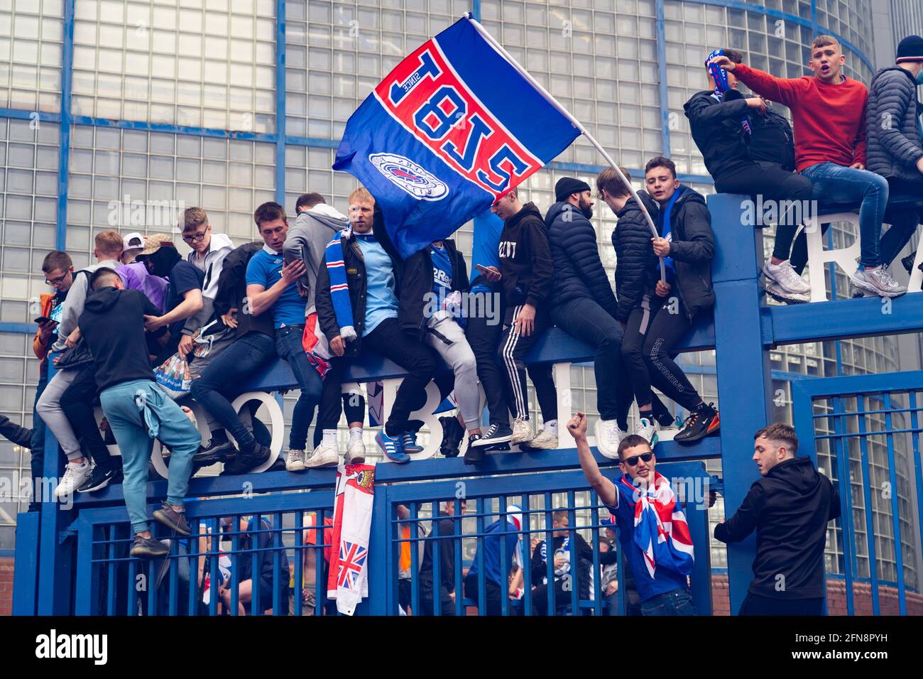 Glasgow, Schottland, Großbritannien. 15 Mai 2021. Tausende von Fans und Fans des Rangers-Fußballvereins kommen im Ibrox Park in Glasgow zusammen, um den Sieg der schottischen Premiership-Meisterschaft zum 55. Mal und zum ersten Mal seit 10 Jahren zu feiern. Rauchbomben und Feuerwerk werden von Fans, die von der Polizei streng kontrolliert werden, weg von den Eingängen des Stadions losgelassen. PIC; Fans feiern nach Vollzeit vor den Toren von Ibriox. Iain Masterton/Alamy Live News Stockfoto