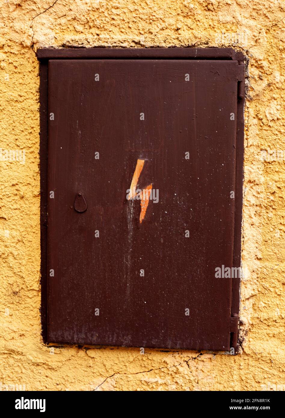 Eine alte elektrische Box mit dem Symbol der Elektrizität, in einer gelben Wand. Stockfoto