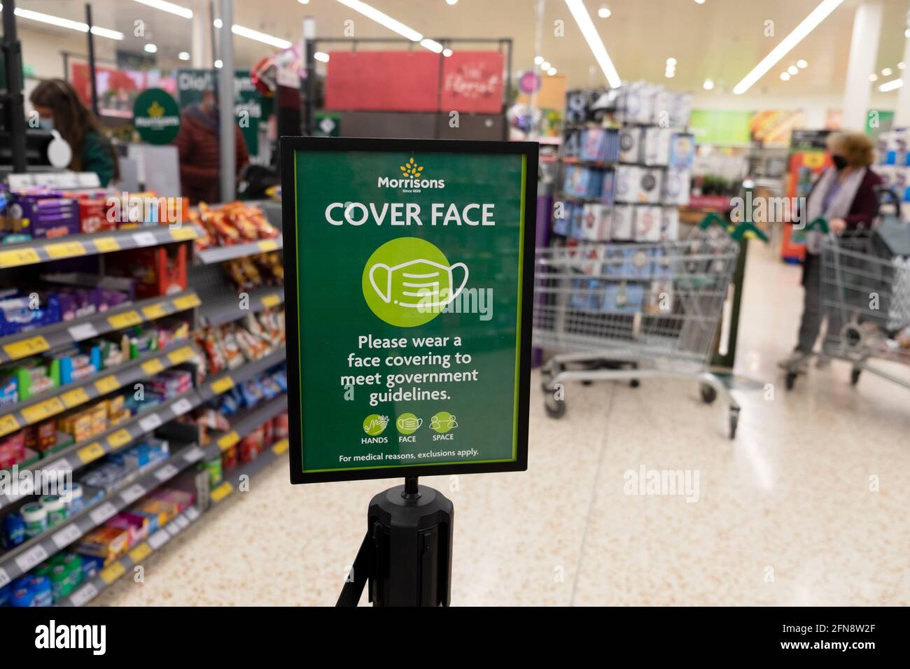 Cover Gesicht mit Gesichtsmaske Regierungsrichtlinien Poster in Gang Während Covid Pandemie in Morrisons Supermarkt Store Inneneinrichtung UK KATHY DEWITT Stockfoto