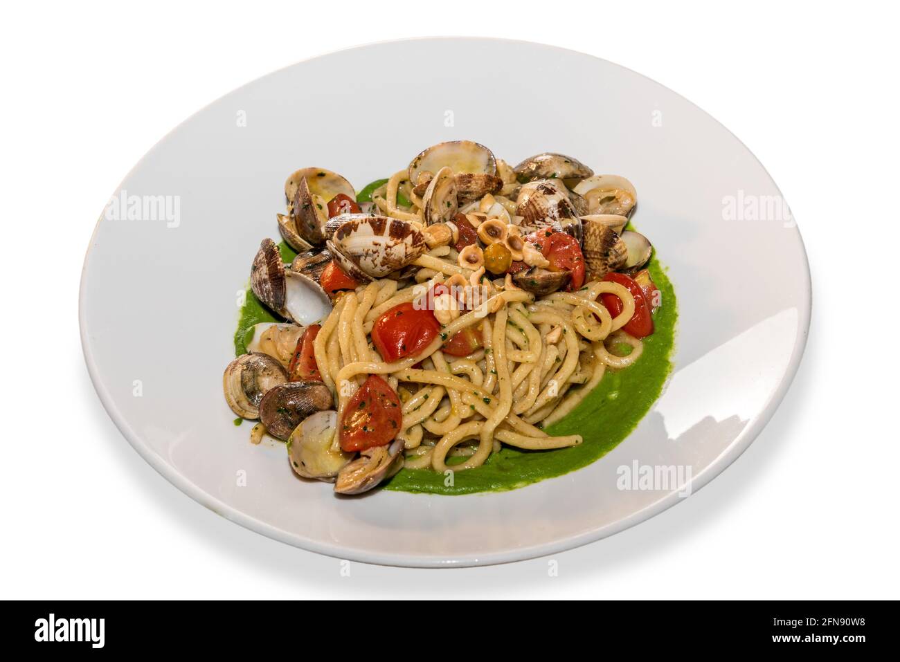 Spaghetti mit Venusmuscheln, Kirschtomaten, Haselnüssen und Gemüsesoße in weißem Teller, isoliert auf Weiß Stockfoto