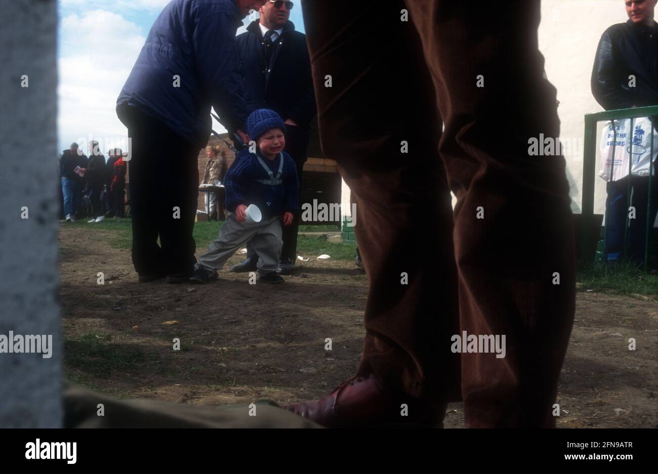 Ein kleines Kind in einem Geschirr ist auf einem Fußballplatz außerhalb der Liga verärgert Stockfoto