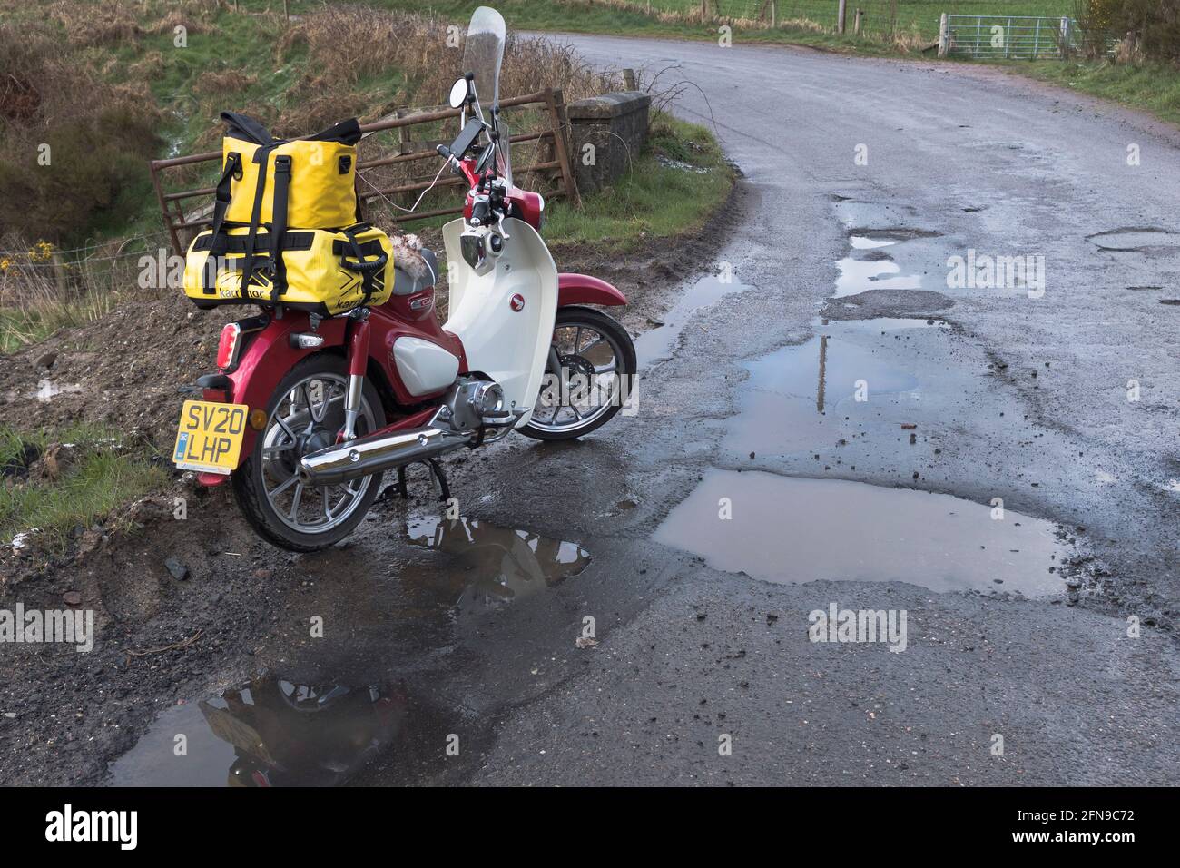 dh Roads SCHOTTLAND UK Schlagloch Motorrad durch Schlaglöcher tiefes Pfütze Loch in beschädigter Straßenoberfläche Covid 19 Winterwetterschaden Nahaufnahme schlechte Fahrbahn Stockfoto