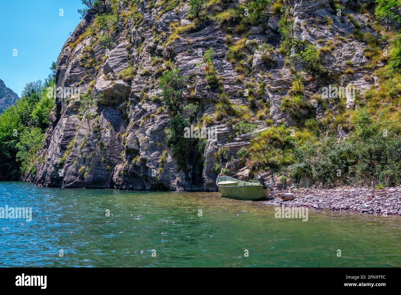 Sommerlandschaft - albanische felsige Berge, bedeckt mit üppigem Laub und See mit ruhigem blauem Wasser, Fischerboot am Ufer Stockfoto